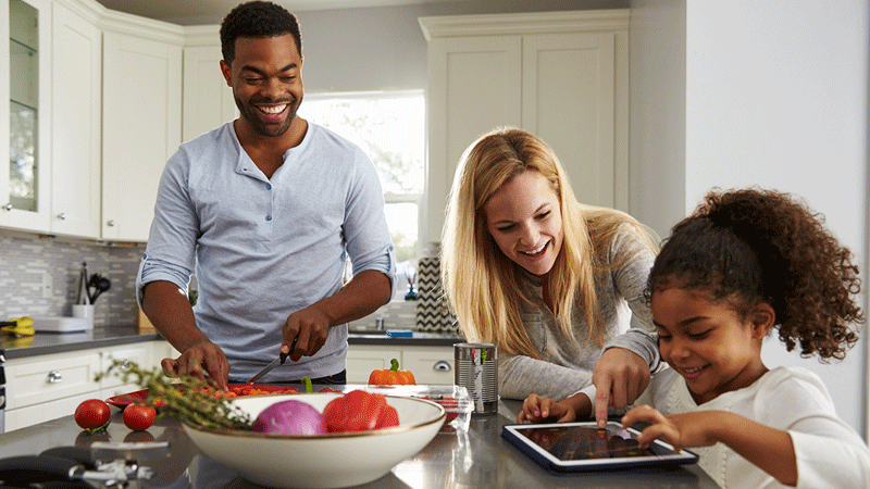 Diverse family eating in kitchen and using tablet